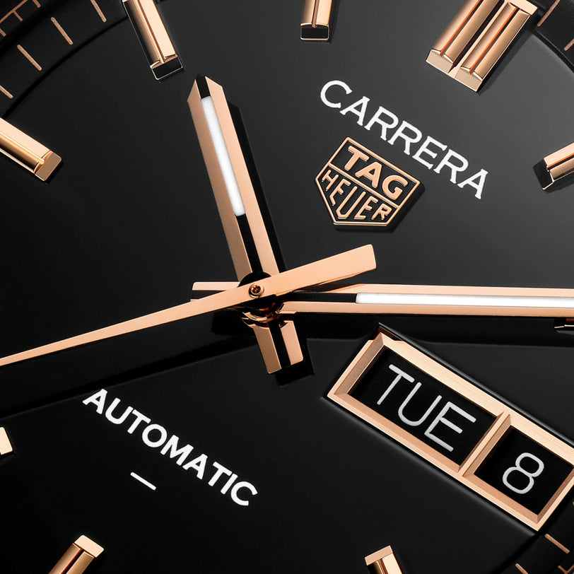 Close-up of the TAG Heuer Carrera Day-Date watch face, featuring gold hands and a day-date display against a black background.