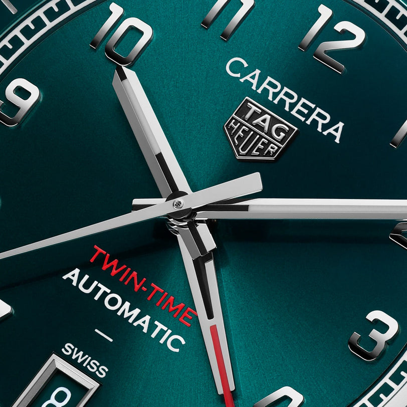 Close-up of a TAG Heuer Carrera Date Twin-Time watch face featuring silver hands and Twin-Time Automatic in red text.