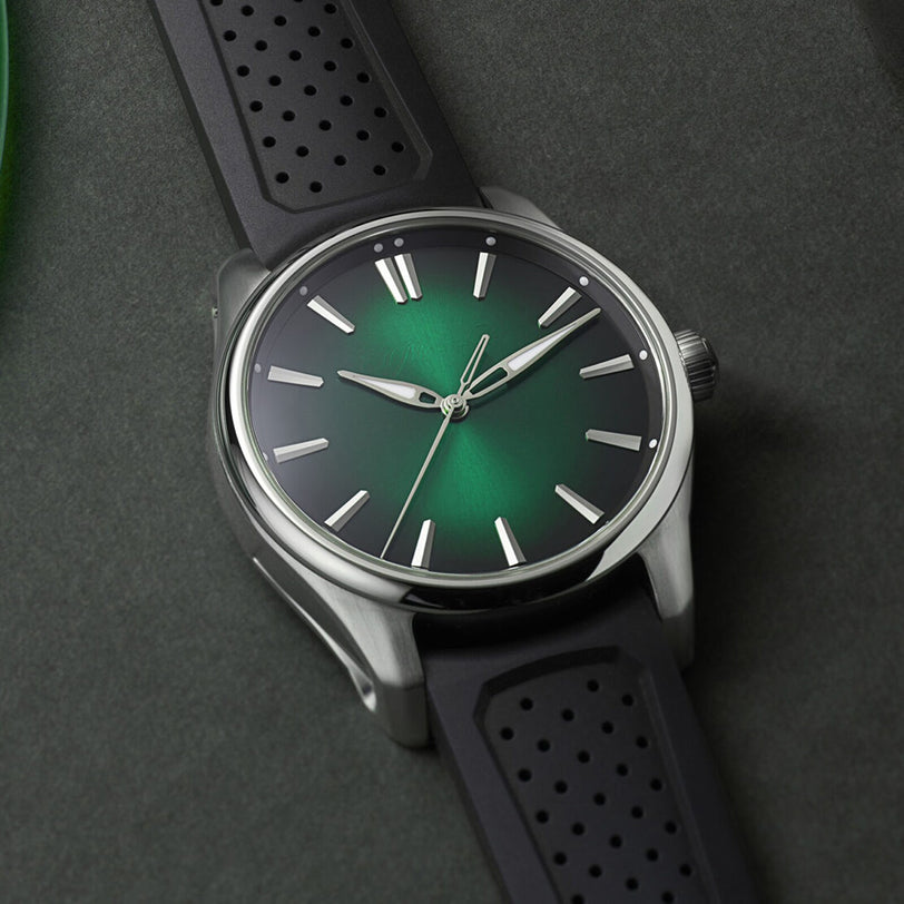 The H. Moser & Cie Pioneer Centre Seconds Cosmic Green features a green gradient dial and black perforated strap, displayed against a dark background.