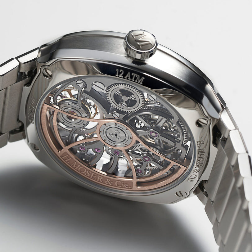 Close-up of the back of the H. Moser & Cie Streamliner Tourbillon Skeleton, showcasing its exposed tourbillon movement and intricate gears, with H. Moser & Cie and 12 ATM labeled on the metal case.