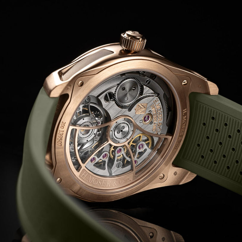 Close-up of the H. Moser & Cie Pioneer Tourbillon Burgundy showing its detailed exposed movement, rose gold case, and green rubber strap.