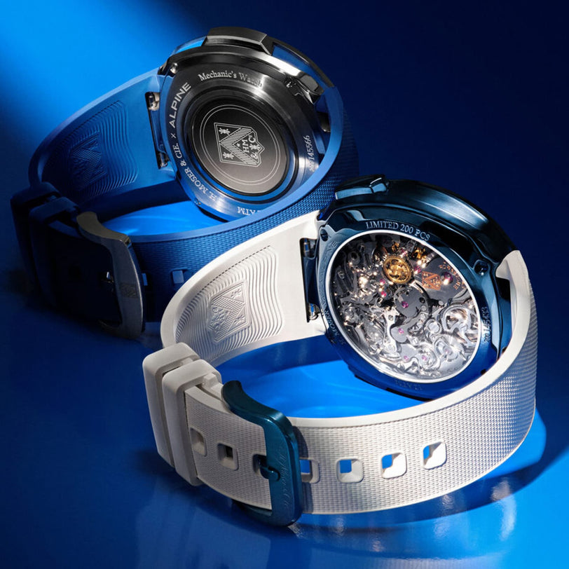 Two H. Moser & Cie Streamliner Alpine Divers Edition watches with blue and white straps are displayed, highlighting their engraved and transparent casebacks.