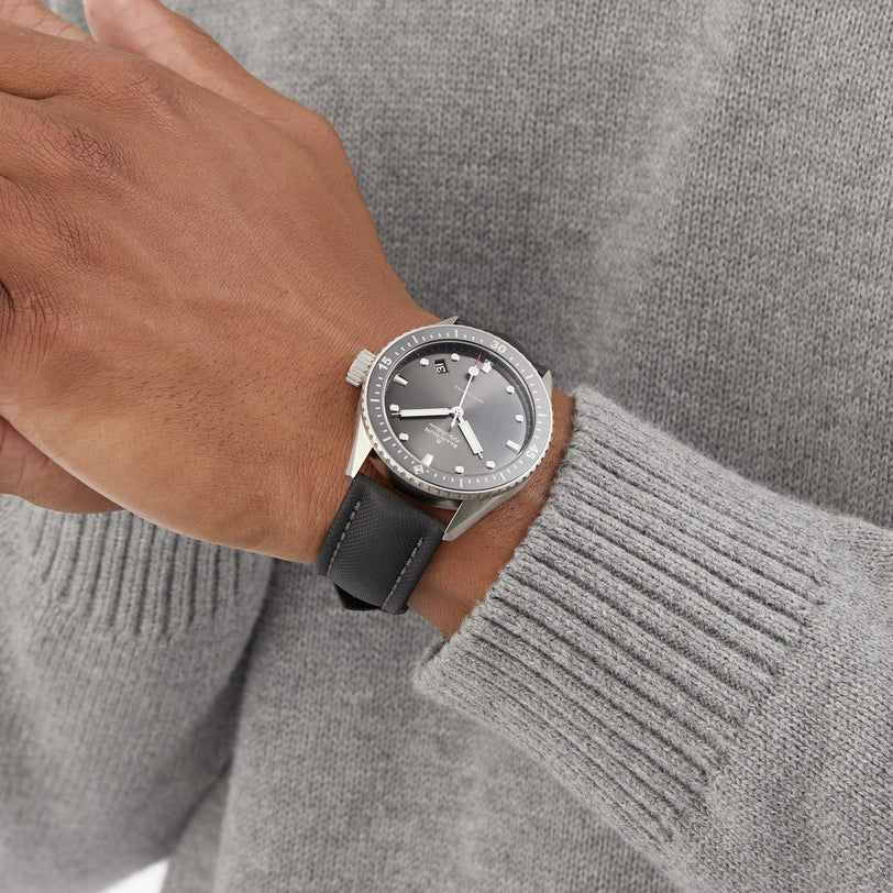 A person wears a gray sweater with a black and silver Blancpain Fifty Fathoms Bathyscaphe, featuring the 1315 calibre automatic movement and displaying the time 10:10.