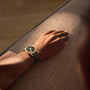 A person wearing a Blancpain Villeret Quantième Phases de Lune with a green strap rests their hand on a textured beige surface.