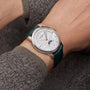 Someone wearing Vacheron Constantins Patrimony Moon Phase Retrograde Date, featuring a silver case in 18K white gold, white dial, green leather strap, date indicator, and precision moon phase display.