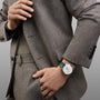 A person in a tweed suit and olive green shirt showcases the Vacheron Constantin Patrimony Moon Phase Retrograde Date, a limited edition watch with a silver moon phase dial and green leather strap, on their left wrist.