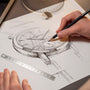 A hand sketches a detailed drawing of the Vacheron Constantin Traditionnelle Manual-Winding wristwatch on paper, with a pencil, ruler, and geometric tools scattered across the desk.