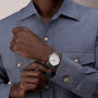 A person in a textured blue-gray button-up shirt showcases a Vacheron Constantin Traditionnelle Manual-Winding platinum watch with a white face on their left wrist.