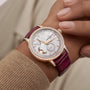 A close-up of a wrist wearing the Vacheron Constantin Traditionnelle Moon Phase in pink gold, featuring a diamond bezel, white dial with gold accents, moon phase display, and a burgundy leather strap.