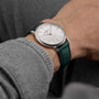 A person wearing the limited edition Vacheron Constantin Patrimony Self-Winding 18K white gold watch with a white dial and green leather strap, dressed in a grey long-sleeve garment.