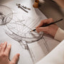 A person sketches a detailed technical drawing of the limited edition Vacheron Constantin Patrimony Self-Winding wristwatch on white paper, with a compass and pencil on the desk.