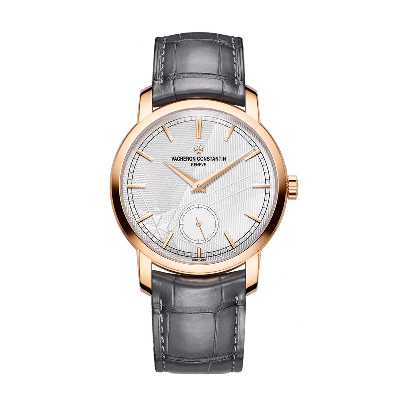 The Vacheron Constantin Traditionnelle Manual-winding, a limited edition 18K pink gold watch with silver dial, black hour markers, small seconds subdial, and gray leather strap is shown elegantly on a white background.