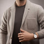 A person in a light gray blazer over a dark t-shirt displays a Vacheron Constantin Traditionnelle Manual-winding watch with a white face and black strap on their left wrist.