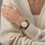 A person in a cream knit sweater crosses their arms, showcasing the limited edition Vacheron Constantin Traditionnelle Manual-winding watch with an 18K pink gold round case and black leather strap.