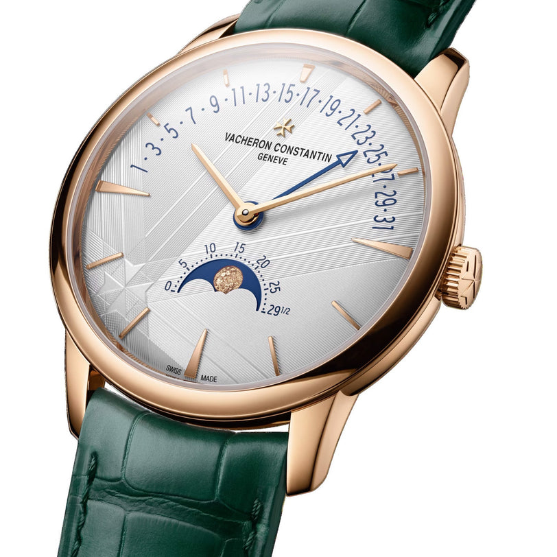 The Vacheron Constantin Patrimony Moon Phase Retrograde Date is a limited edition wristwatch in 18K pink gold, with a green leather strap, white dial, gold markers, retrograde date display, and a moon phase at 6 o’clock.