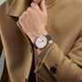 A person in a tan coat displays their wrist adorned with the Vacheron Constantin Patrimony Moon Phase Retrograde Date, a limited edition watch featuring a round white face, green strap, and retrograde date display.
