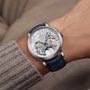A close-up of a wrist wearing the Vacheron Constantin Traditionnelle Perpetual Calendar Retrograde Date Openface, a platinum timepiece with a blue leather strap, showcasing its skeleton-style design and visible self-winding movement.