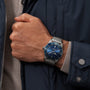 A person in a navy jacket and light beige sweater wears a Breitling Superocean Heritage B20 Automatic 46 watch with a blue dial and mesh metal strap.