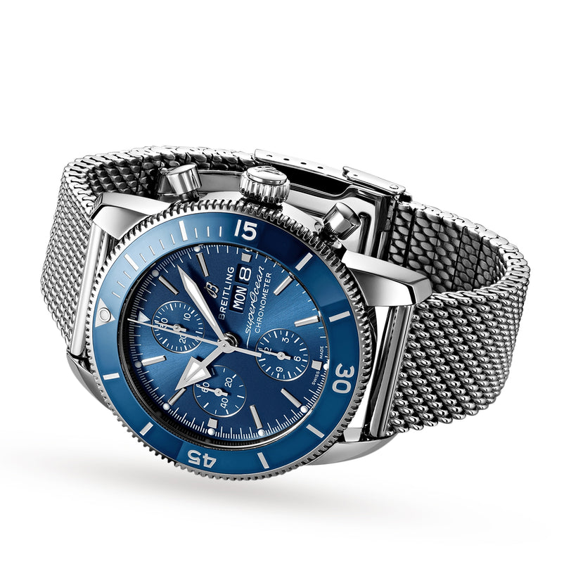 The Breitling Superocean Heritage Chronograph 44 features a stainless steel case, blue dial and bezel, and a stainless steel mesh bracelet, shown against a white background.