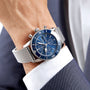 A person in a navy blue suit and white shirt wears the Breitling Superocean Heritage Chronograph 44 with a blue dial and stainless steel mesh bracelet.