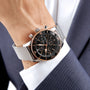 A close-up of a person in a navy suit and white shirt wearing a Breitling Superocean Heritage B20 Automatic 44 with a stainless steel case, black dial, and mesh strap.