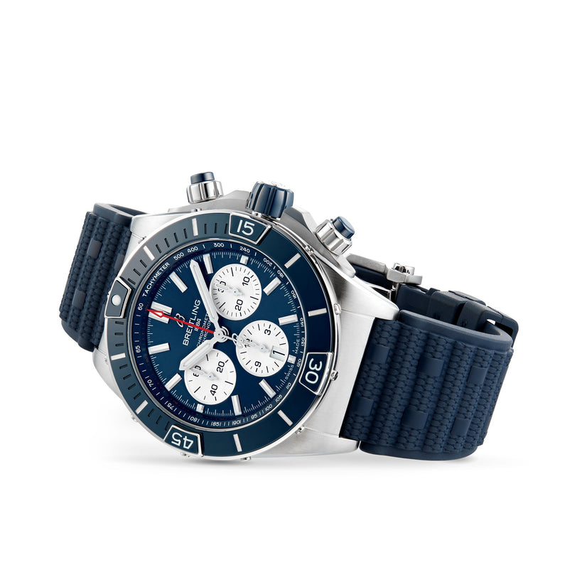 The Breitling Super Chronomat B01 44 is a stainless steel mechanical chronograph featuring a blue dial with three subdials, a rotating bezel, and a textured blue rubber strap.
