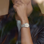 A person wearing a Breitling Chronomat 32 with a diamond-set bezel rests their hand near their chin, dressed in a dark, buttoned-up shirt.