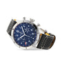 The Breitling Super AVI B04 Chronograph GMT 46 Tribute To Vought F4U features a stainless steel case, blue chronograph dial with three subdials, and a black leather strap with white stitching, displayed at an elegant angle.