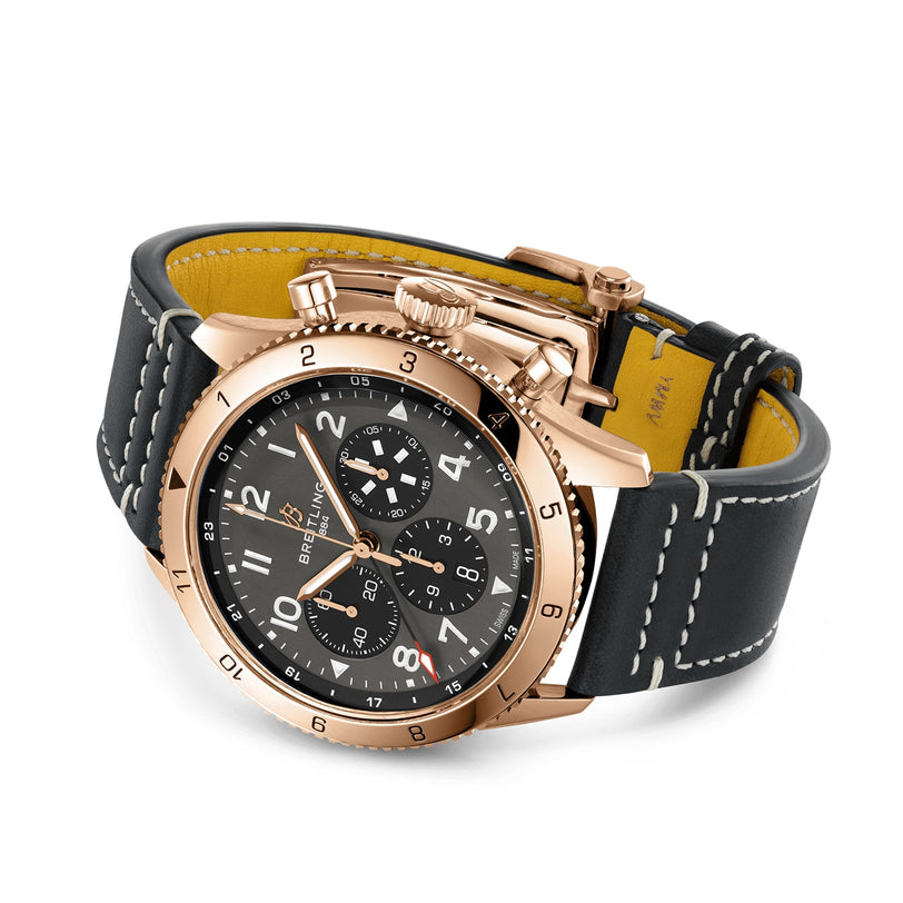 The Breitling Super AVI B04 Chronograph GMT 46 P-51 Mustang features a rose gold case, black dial with multiple subdials and white numerals, plus a black leather strap with white stitching—inspired by aviation heritage.