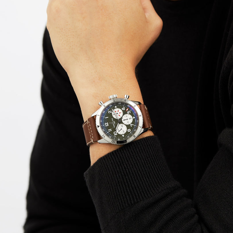A person in a black long-sleeve top showcases the Breitling Super AVI B04 Chronograph GMT 46 Curtiss Warhawk, featuring a brown leather strap and black dial, celebrating aviation heritage.