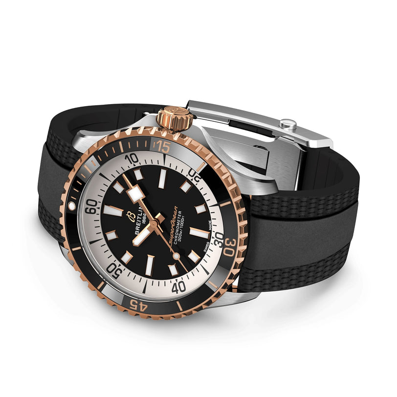 The Breitling Superocean Automatic 42, inspired by the 1960s Slow Motion era, features a black and gold round face, black bezel with white markers, and a black rubber strap. Its displayed at an angle.