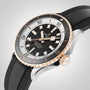 A Breitling Superocean Automatic 42 dive watch with a black dial, gold bezel, and black rubber strap is displayed on a light gray background.
