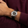 A person wearing a Breitling Superocean Automatic 42 wristwatch with a black strap and black and silver details, paired with a burgundy sweater.