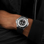 A person wearing a Breitling Superocean Automatic 46 black and silver wristwatch with a black strap and a black jacket.