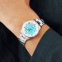 A person wears a Breitling Superocean Automatic 36 diving watch with a silver case, turquoise dial, and silver markers, paired with a dark long-sleeve shirt.