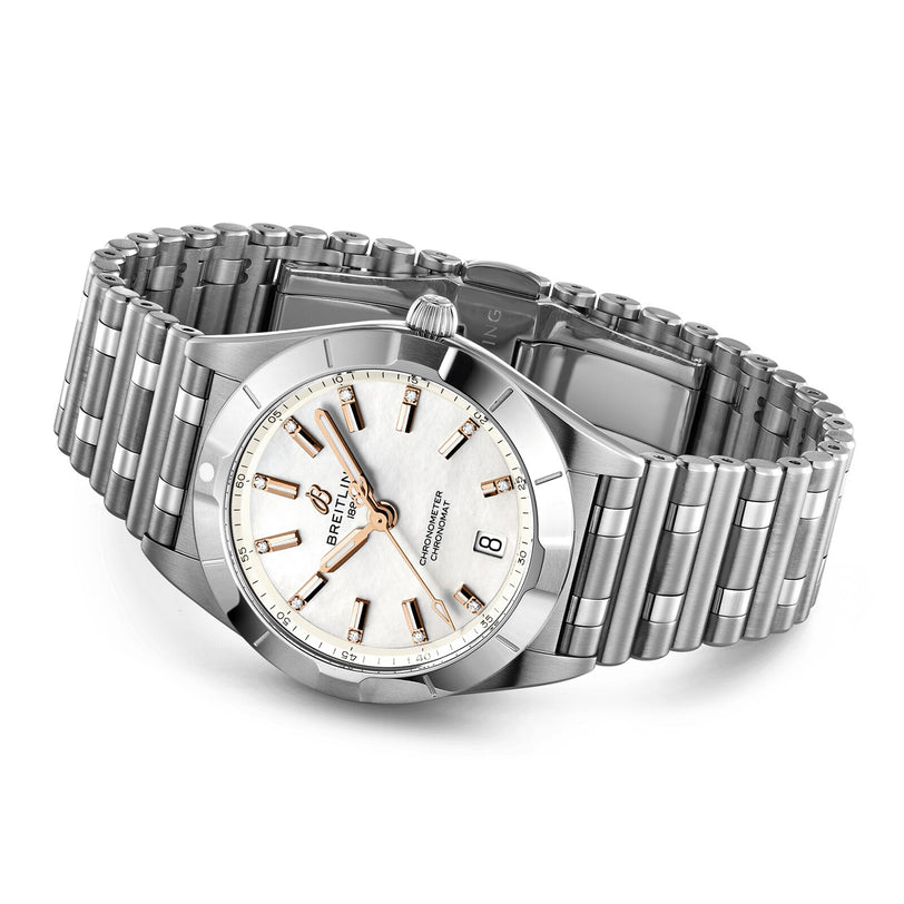 The Breitling Chronomat 32 is a stainless steel wristwatch featuring a silver link bracelet, mother of pearl dial, gold hour markers, date window at 3 o’clock, and a textured crown.