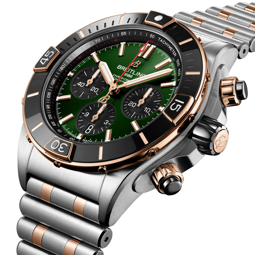 A close-up of the Breitling Super Chronomat B01 44, a luxury chronograph watch with an emerald dial, black bezel, and a silver and rose gold metal bracelet.