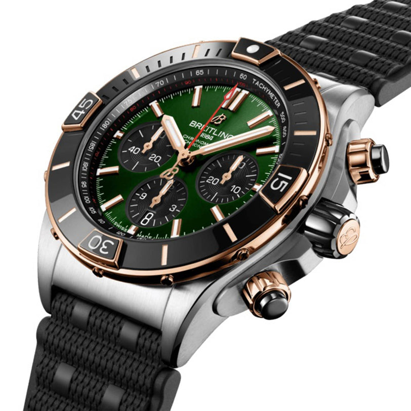The Breitling Super Chronomat B01 44 is a luxury chronograph wristwatch with a green dial, black bezel, gold accents, three subdials, a black textured strap, and precise Breitling 01 calibre movement, shown from an angled view.