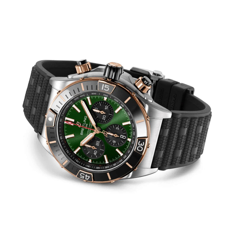 The Breitling Super Chronomat B01 44 is a stainless steel and gold chronograph with a green dial, black bezel, black textured rubber strap, two side pushers, and is powered by the Breitling 01 calibre.