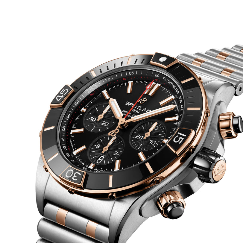 A close-up of the Breitling Super Chronomat B01 44 wristwatch, featuring a black dial, 18ct rose gold and silver accents, and a metal bracelet. COSC certified for precision.