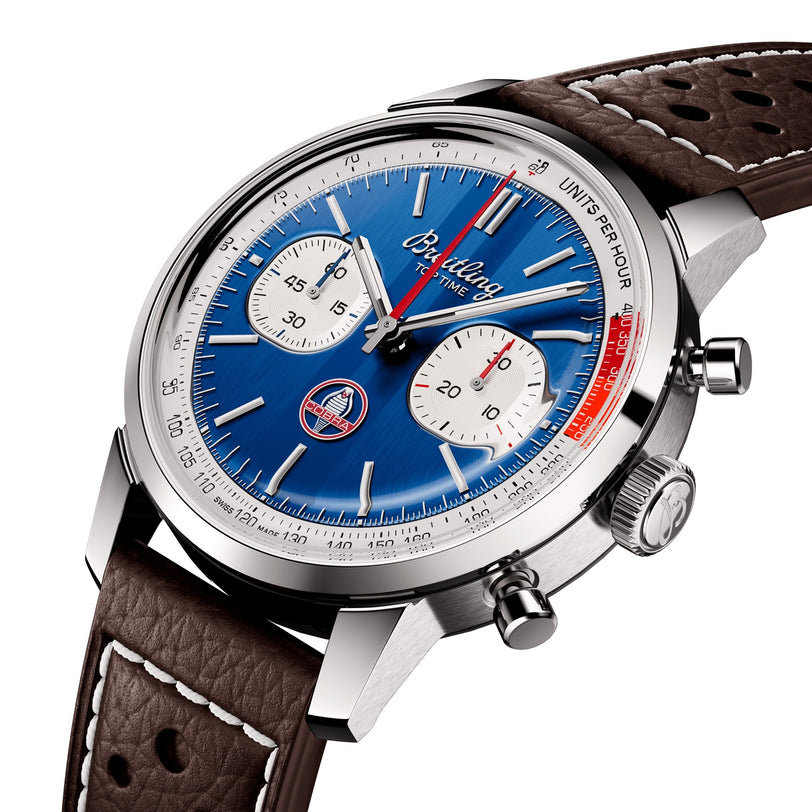 Close-up of the Breitling Top Time B01 Shelby Cobra, featuring a blue dial with white subdials, stainless steel case, and brown perforated leather strap. The Breitling brand is visible on the watch face.