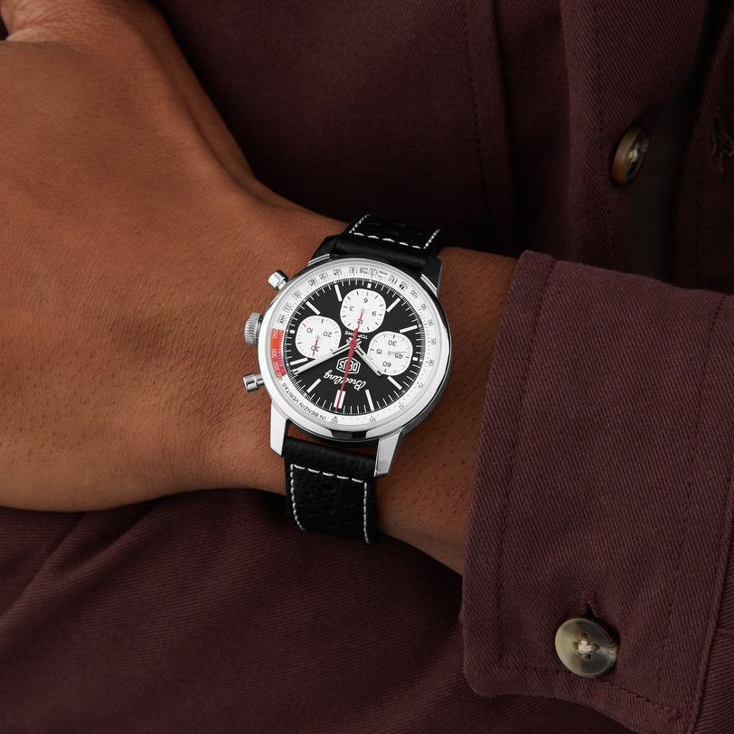 A person wearing a Breitling Top Time B01 Deus silver and black racing chronograph with a black leather strap, resting their hand on a maroon shirt.