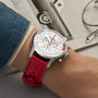 Someone wearing a Breitling Top Time B01 Ford Thunderbird chronograph with a white dial and red leather strap is shown near a grayscale photo of a Ford Thunderbird.