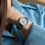 A person wearing a light blue collared shirt and a Breitling Navitimer 32 wristwatch with a blue mother of pearl dial, diamond hour markers, and a matching blue leather strap.