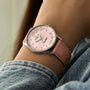 A person dressed in a light denim jacket wears the Breitling Navitimer 32, featuring diamond hour markers, a pink face, and a pink leather strap.