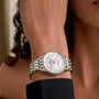 A person wears a Breitling Navitimer 32, a silver wristwatch with a white dial and diamond hour markers featuring SuperQuartz™ movement, on their left wrist, shown from the side against a neutral background.
