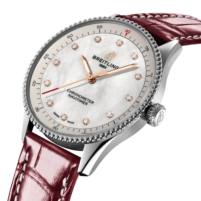 A silver Breitling Navitimer 32 watch with a diamond-studded white dial and red leather strap, powered by the Breitling Calibre 77, is displayed at an angle on a white background.