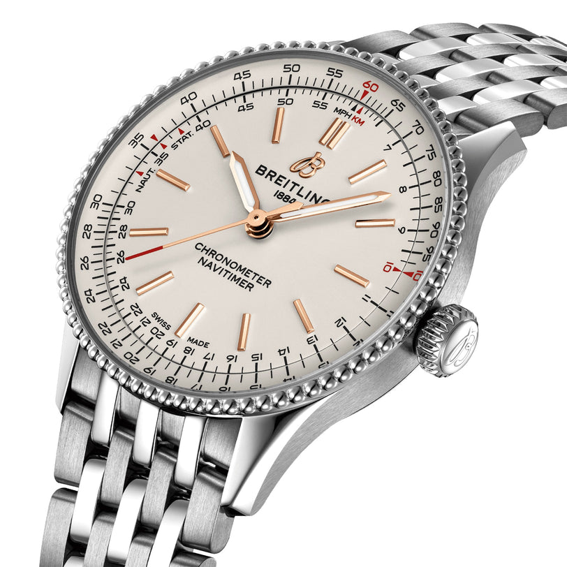 A close-up of the Breitling Navitimer Automatic 36 showcases its silver metal band, white dial, gold hour markers, three hands, and detailed chronograph markings with iconic branding.
