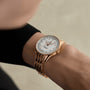 Photographed from above against a neutral background, a person wears the Breitling Navitimer Automatic 36 in rose gold with a white dial and gold hour markers.