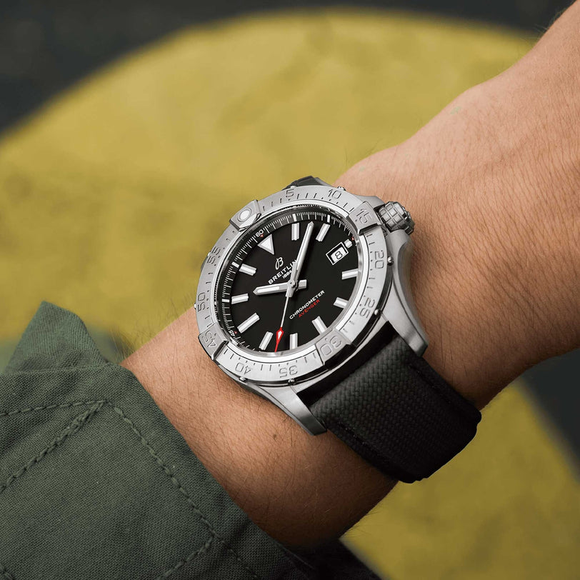 A close-up of a wrist wearing the Breitling Avenger Automatic 42, featuring a stainless steel case, black textured strap, and paired with a dark green long-sleeve shirt.
